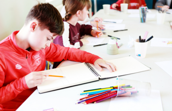 A young person is drawing in a sketchbook with colouring pencils