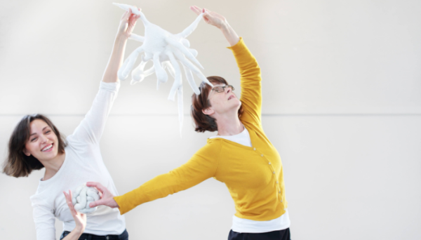 Two people are holding a white abstract sculpture and are engaged in a dance.