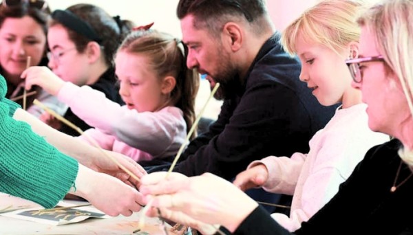 A group of people of various ages are gathered around a table, engaged in a craft activity.