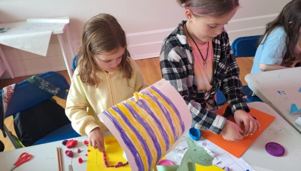 Two children making viking ships with coloured paper