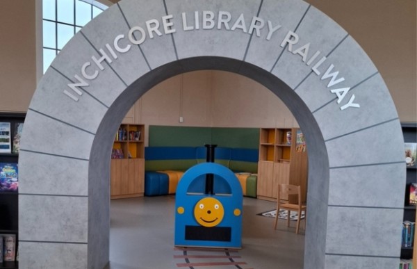 A stone archway with Inchicore Library Railway inscribed on it, leading to a children's play area with a blue train and colourful seating.