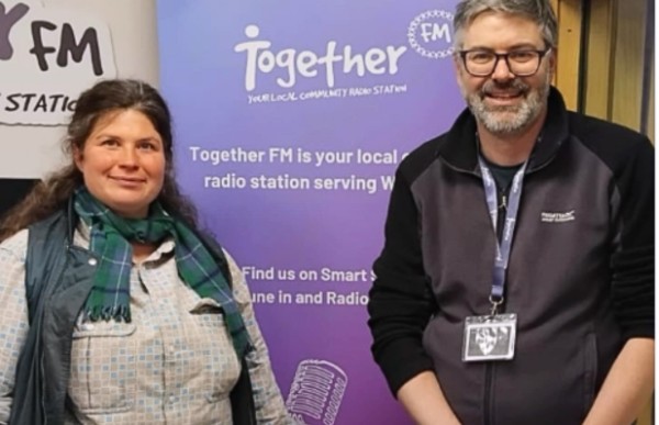 Two people standing in front of a sign with the words 'Together FM'