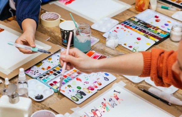 a group of people sitting at a table with watercolors and paints