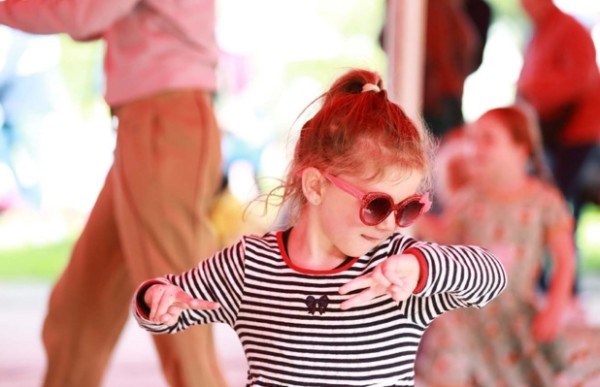 A young child wearing pink heart-shaped sunglasses dancing