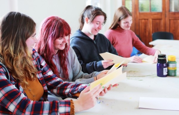 Four young adults sitting at a table together and working with paper and paints
