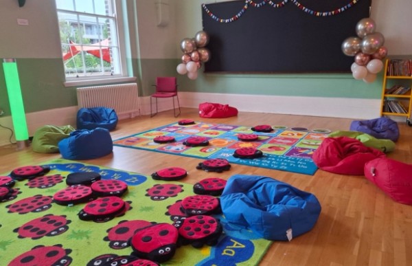 A classroom with beanbag chairs, colourful rugs featuring ladybugs and alphabet letters. 