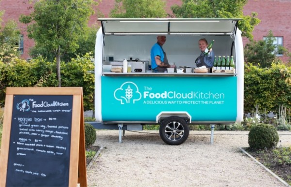A food truck in a courtyard with the name 'FoodCloud Kitchen. Two adults are in the truck, smiling at the camera.