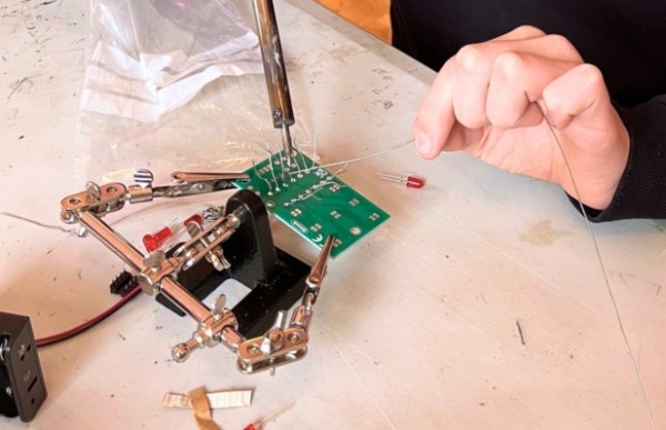 A close up of a person's hand is soldering onto a small circuit board