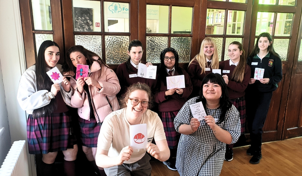 A group of students and two adults in a classroom holding up drawings