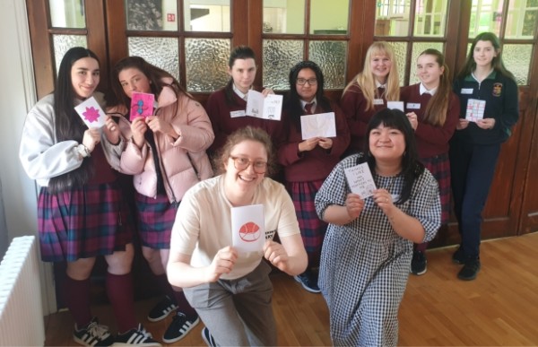 A group of young people in school uniform hold up cards with drawings