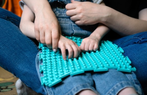 A child's arms playing with a sensory toy, helped by an adult. 
