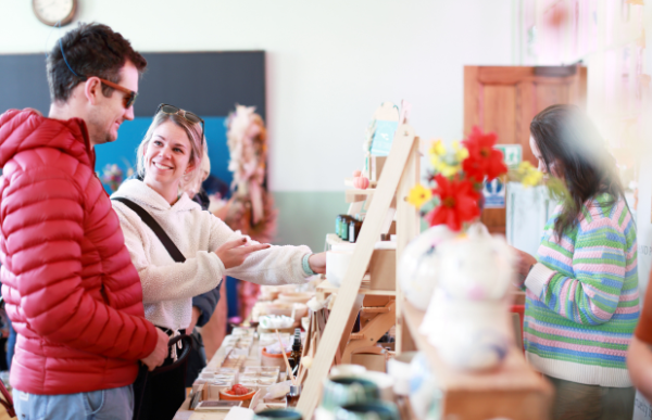 Two people smiling and looking at a display of goods at a market.