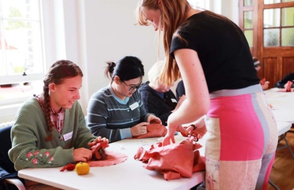 A number of people sitting at a table working with textiles